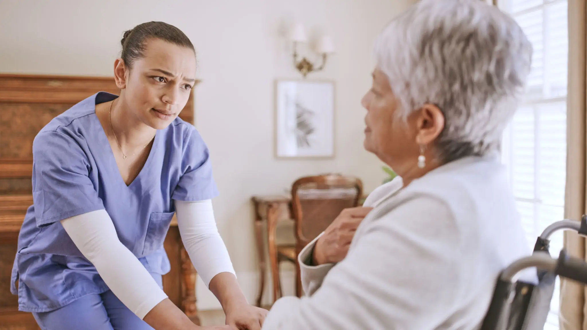 A nurse attentively listens to an elderly woman in a cozy living room.