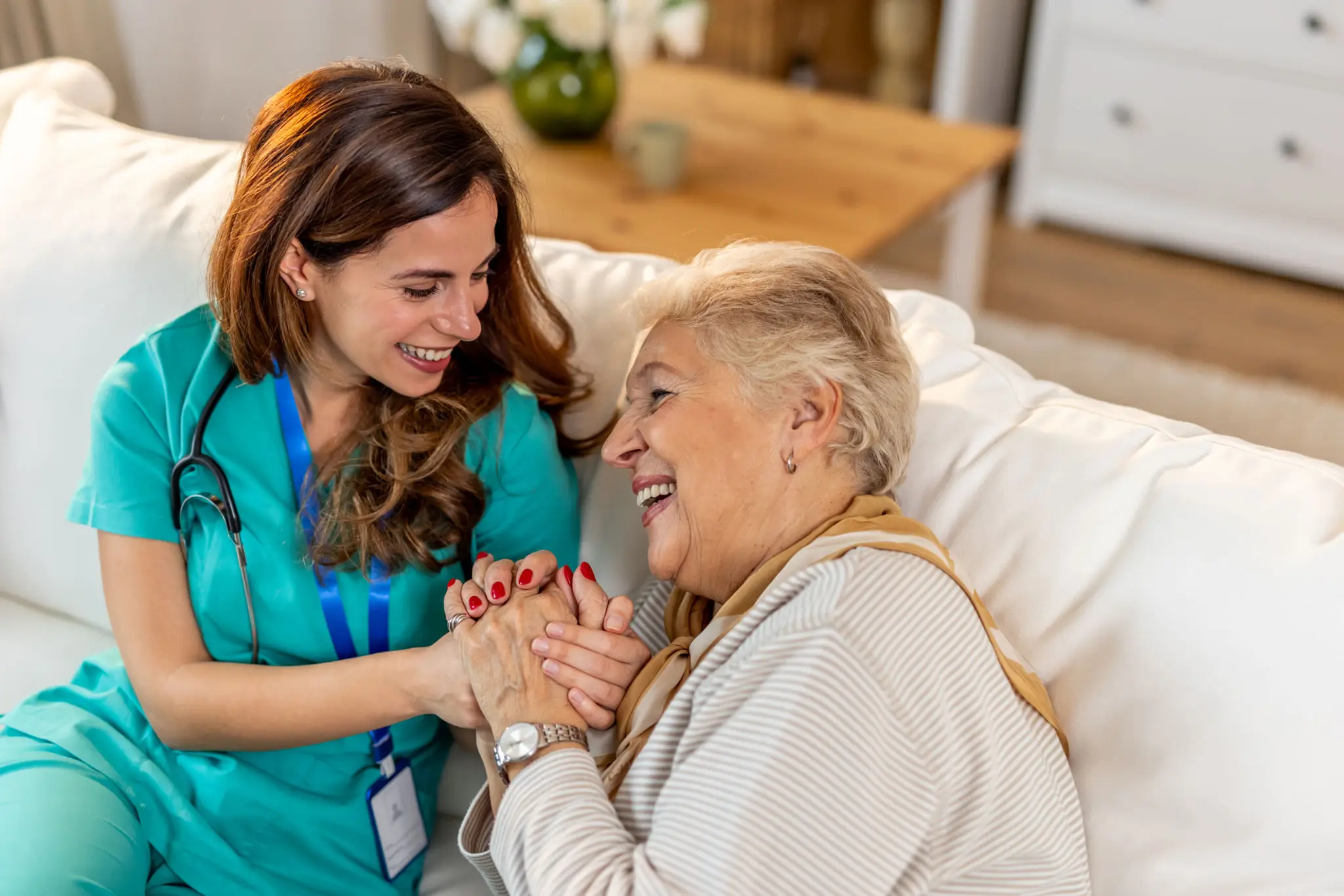 Caregiver and elderly woman sharing a joyful moment on the couch.