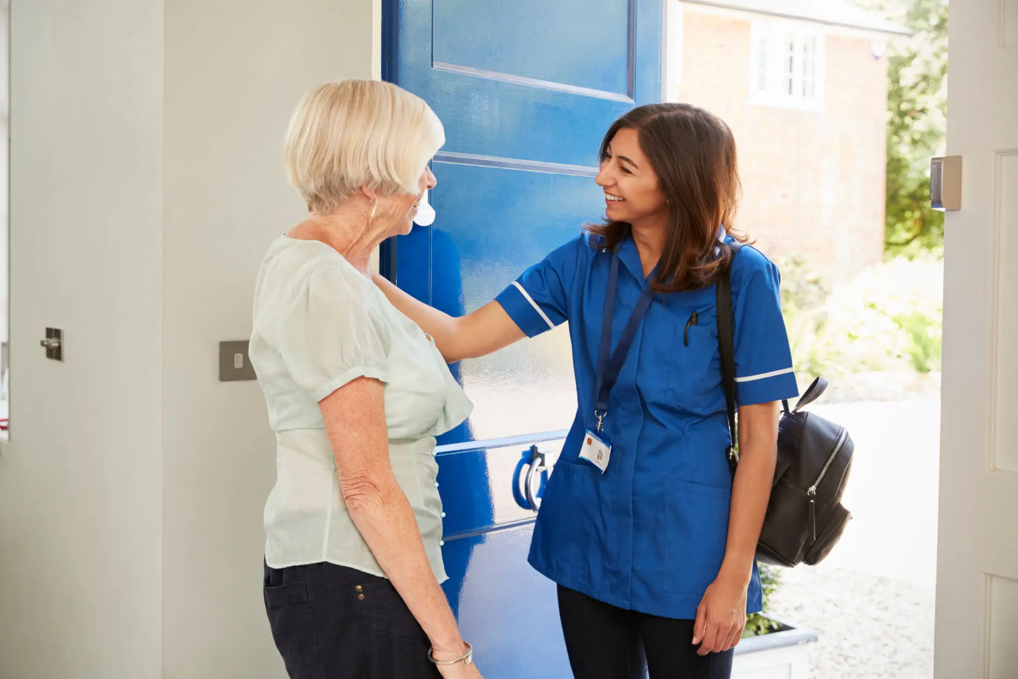 Nurse greeting elderly woman at her door with warmth.
