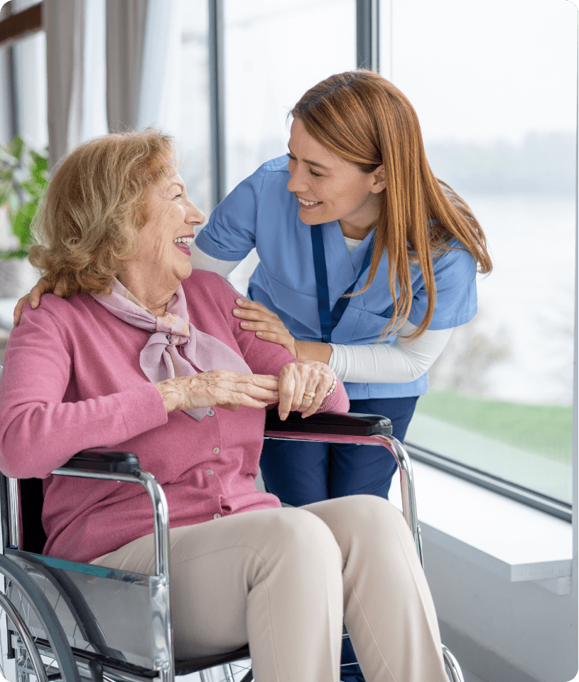 Elderly woman in wheelchair with caregiver smiling.